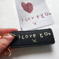 Black keychain with 'I love you' text held by a hand, with a small card in the background.