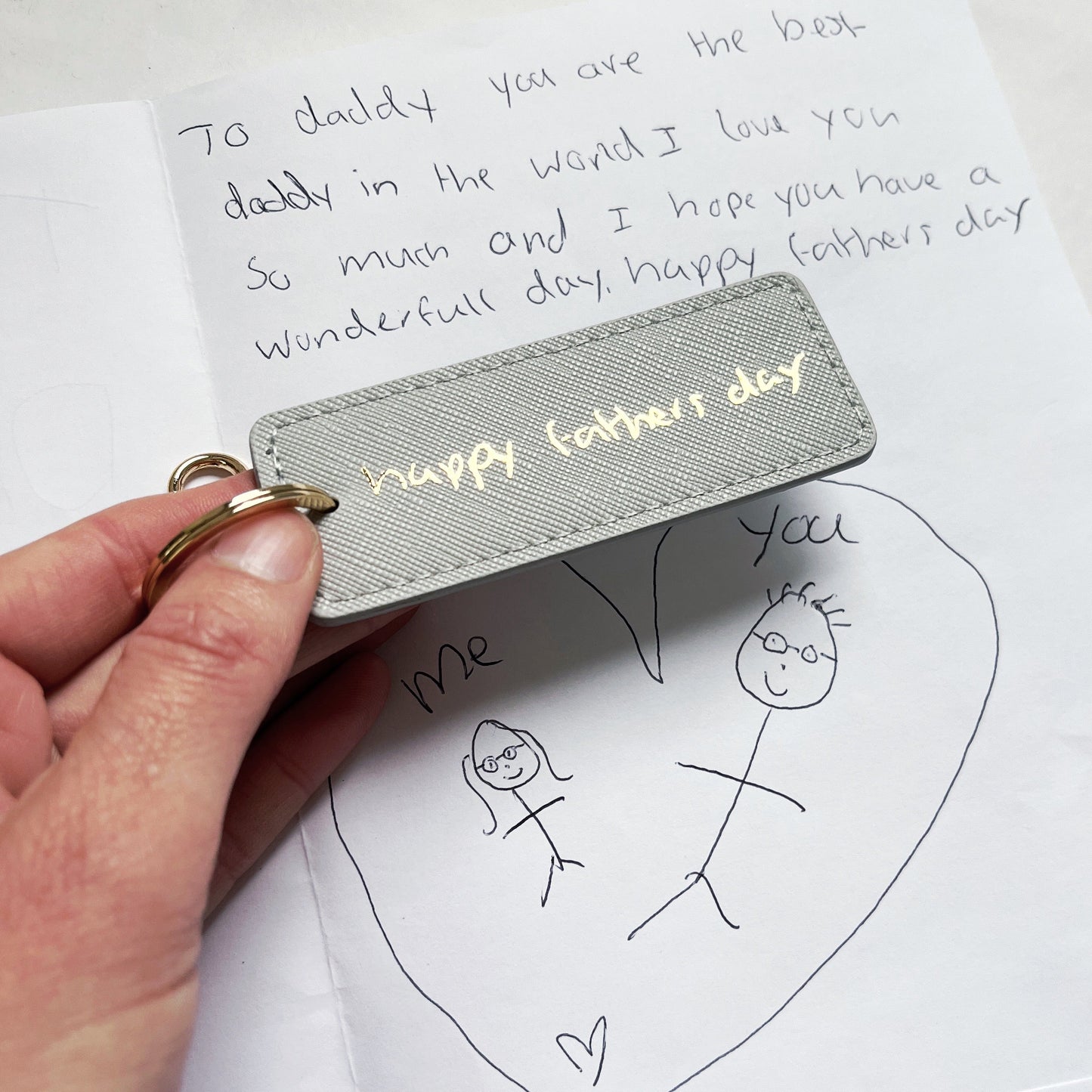 Handwritten card with a fathers day keyring and a child's drawing on a white background